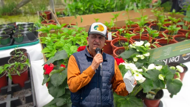 Khurshid Chishti holding a microphone against a background of potted plants